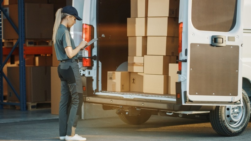  Mujer haciendo inventario de pedidos en furgoneta delante de un almacén
