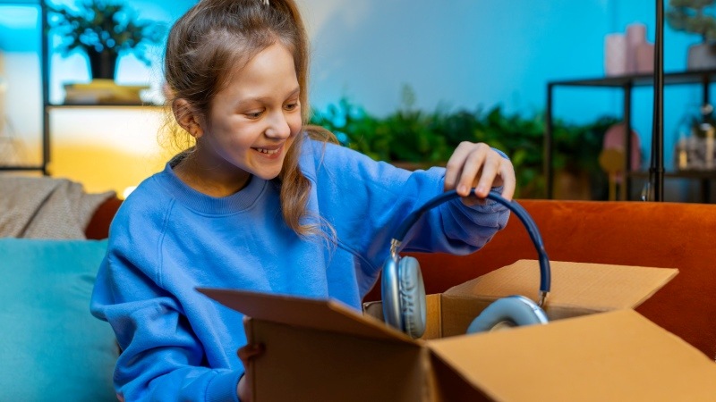 Niña abriendo una caja de cartón sacando unos auriculares