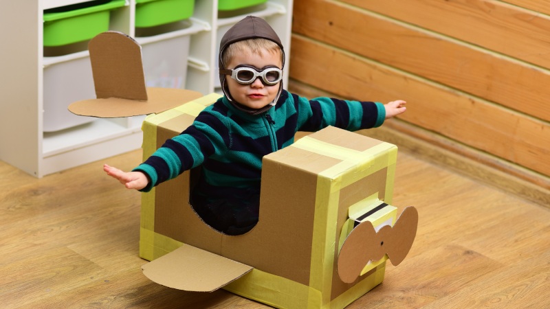 Niño jugando con caja de cartón convertida en avión