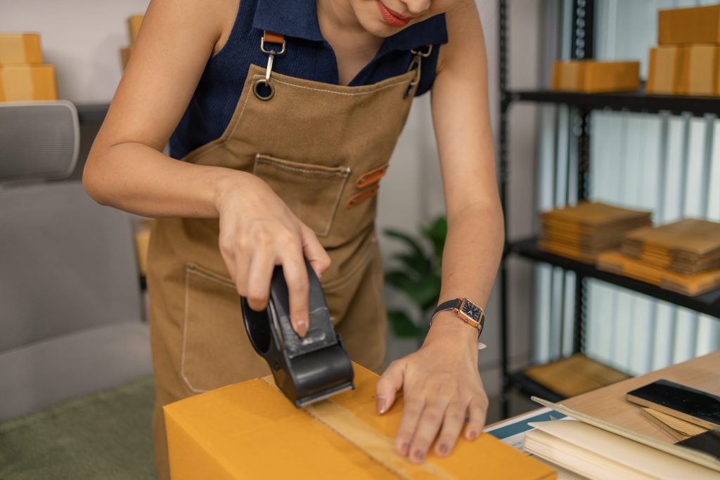 Mujer sellando una caja de cartón con cinta adhesiva haciendo presión